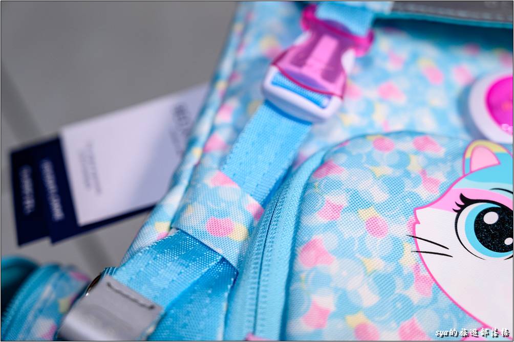 書包前方的束帶一方面可以收納上蓋背袋的調整帶，同時尾端是個顯眼的反光設計。